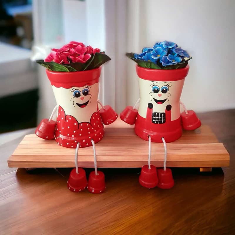 Dois vasos articulados decorativos com flores vermelhas e azuis em suporte de madeira